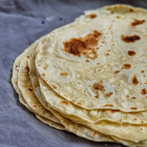 Stack of Sonoran tortillas de harina with golden brown spots on grey linen