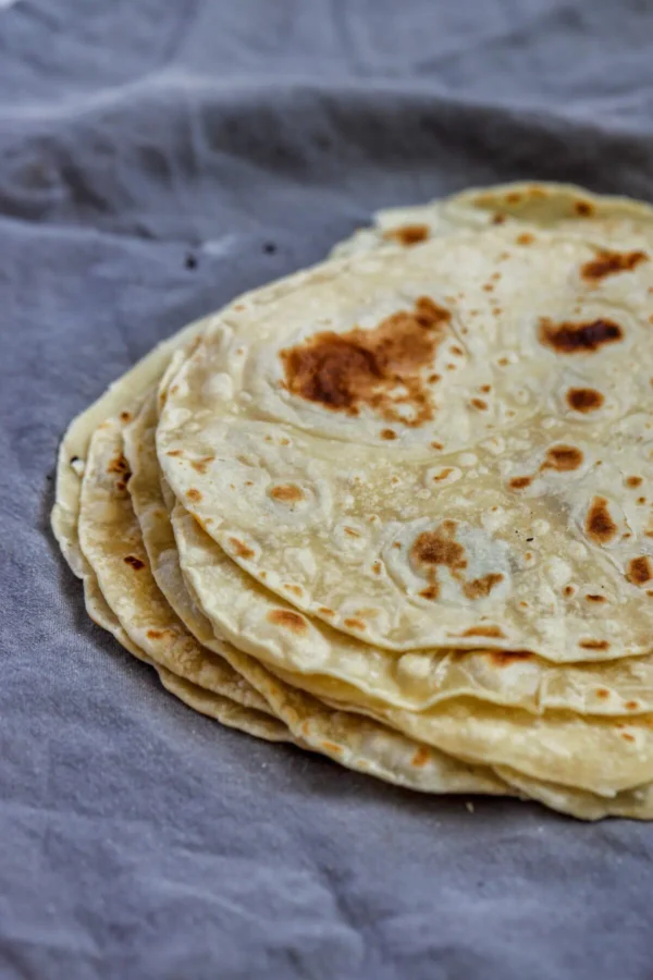 Stack of Sonoran tortillas de harina with golden brown spots on grey linen