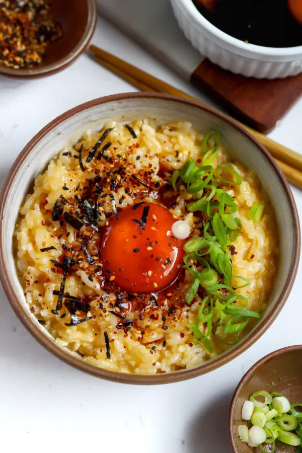 A bowl of creamy Japanese Tamago Kake Gohan topped with a glossy soy-cured yolk, furikake, and curled green onions.