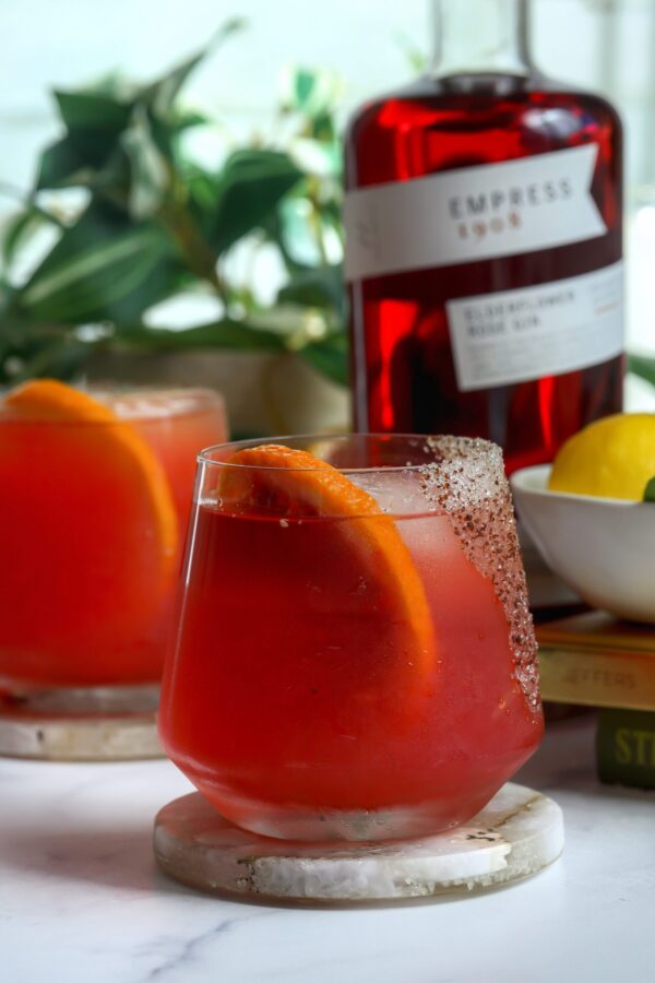 Prickly pear cocktail made with empress gin, with a spicy sugar Rin and a blood orange for garnish.