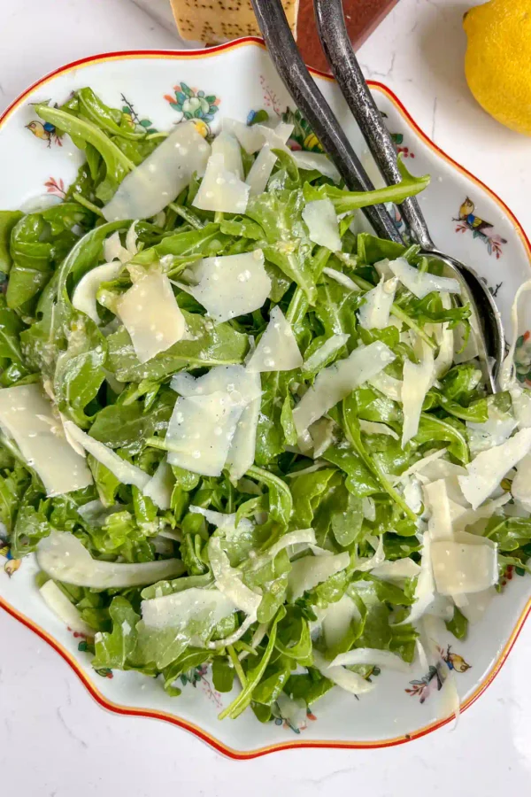 A bowl of arugula fennel salad tossed with honey dijon dressing and shaved parmesan.