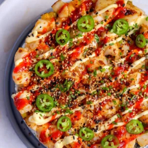 Slice of baked sushi cake showing layers of seasoned rice, toasted nori, cucumber, and avocado under broiled spicy scallops.