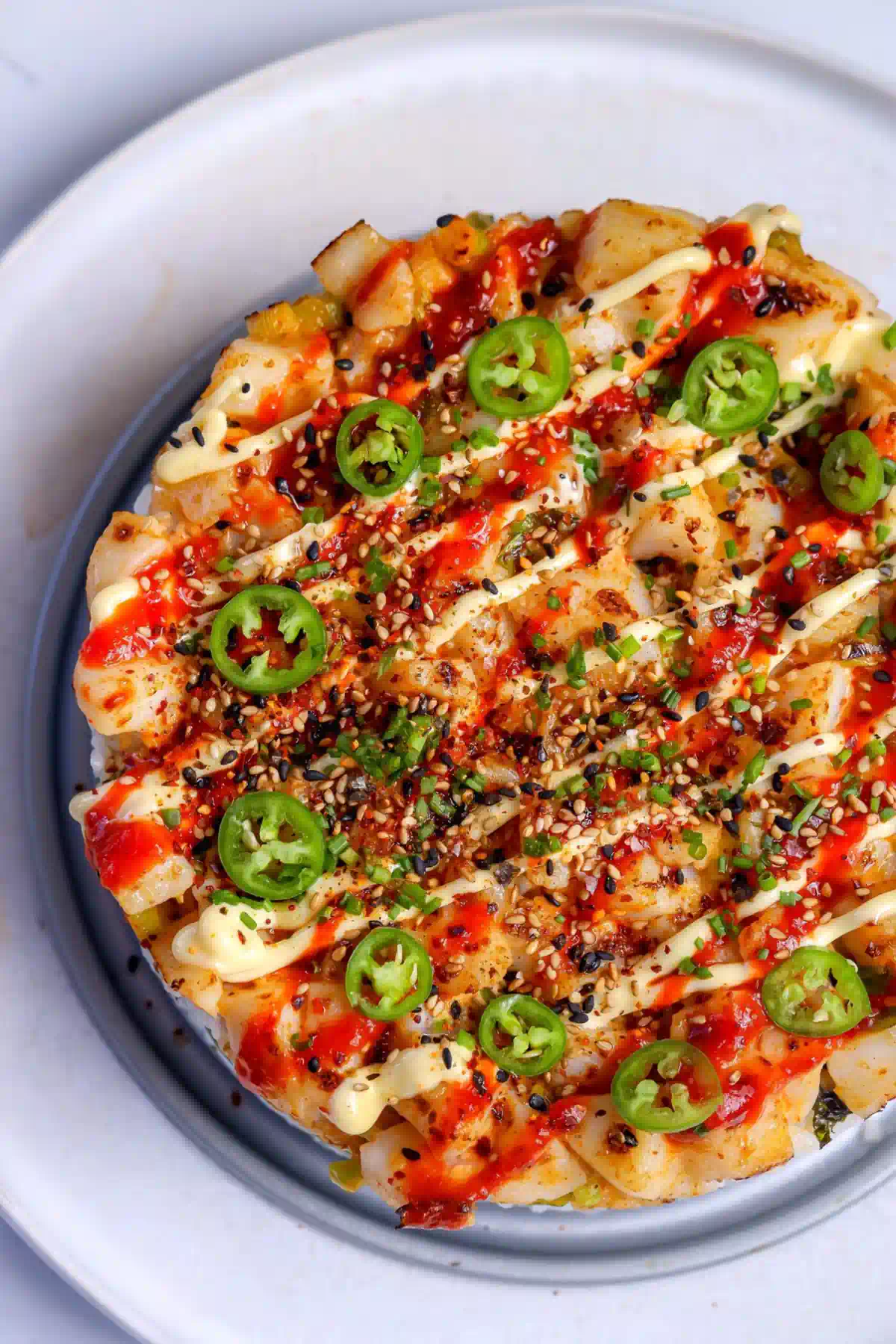 Slice of baked sushi cake showing layers of seasoned rice, toasted nori, cucumber, and avocado under broiled spicy scallops.