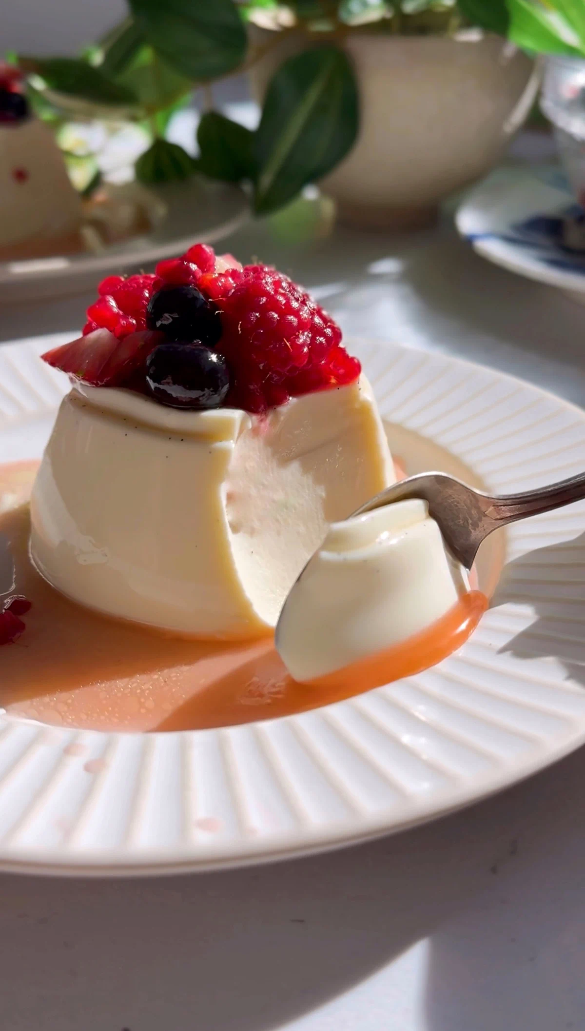 Spoon lifting a bite of berry panna cotta with macerated berry juices pooled on the plate.