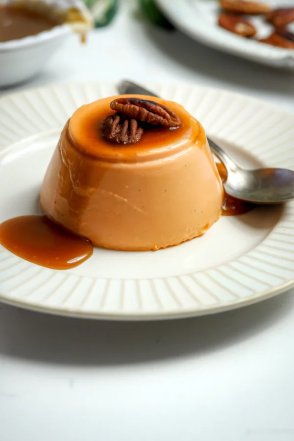 Unmolded carrot cake panna cotta on a white plate with bourbon butterscotch dripping down the sides and a pecan half on top