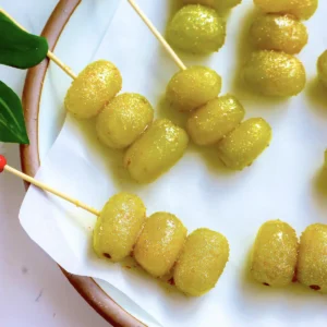 Champagne grapes rolled in gold sugar and threaded onto wooden skewers, plated on parchment with red berries and green leaves