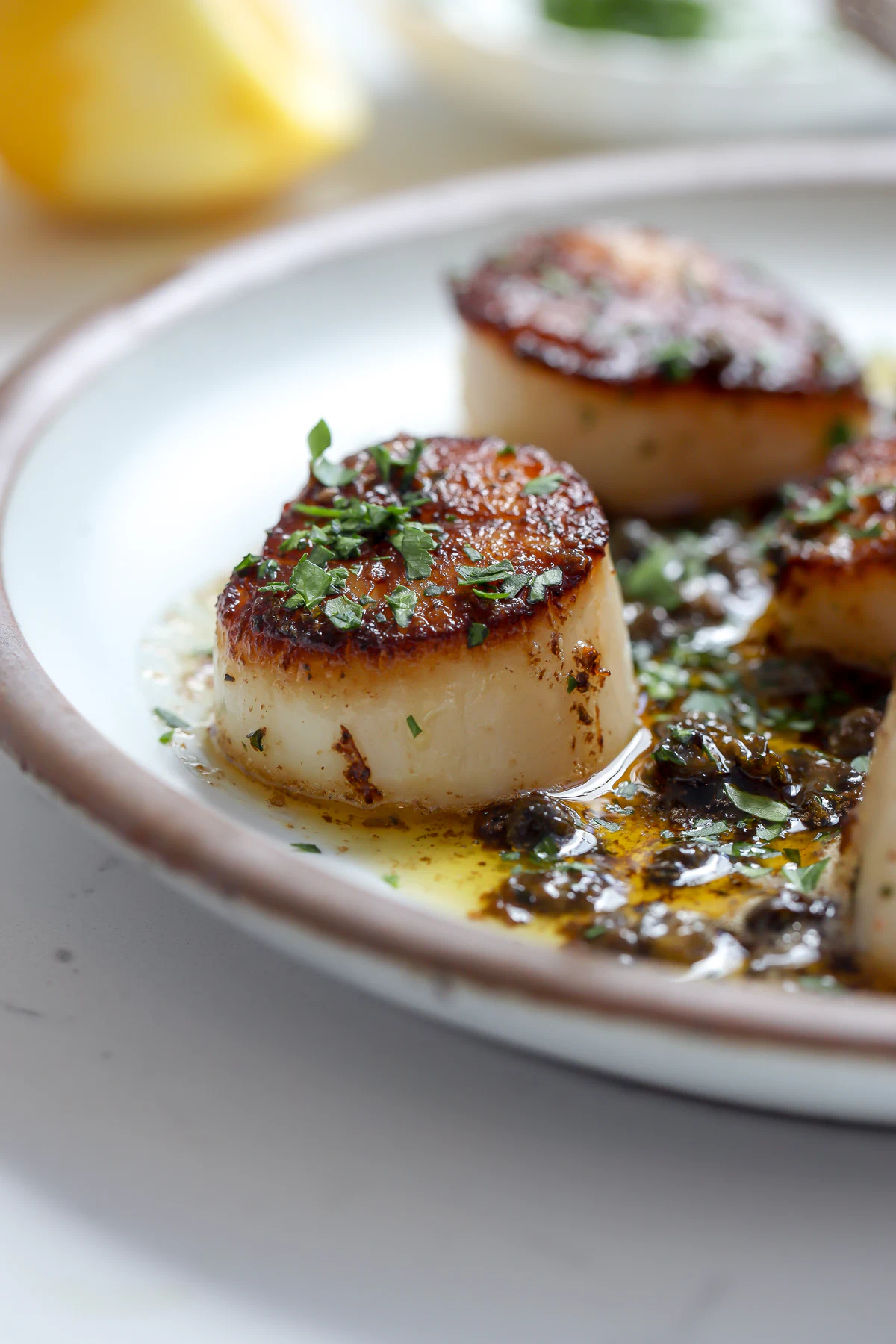 Close-up of a pan-seared scallop meunière with a deep golden crust and lemon caper butter sauce