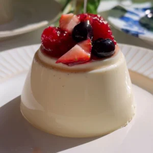 Close-up of berry panna cotta topped with raspberries, blueberries, and strawberries as syrup is spooned over.