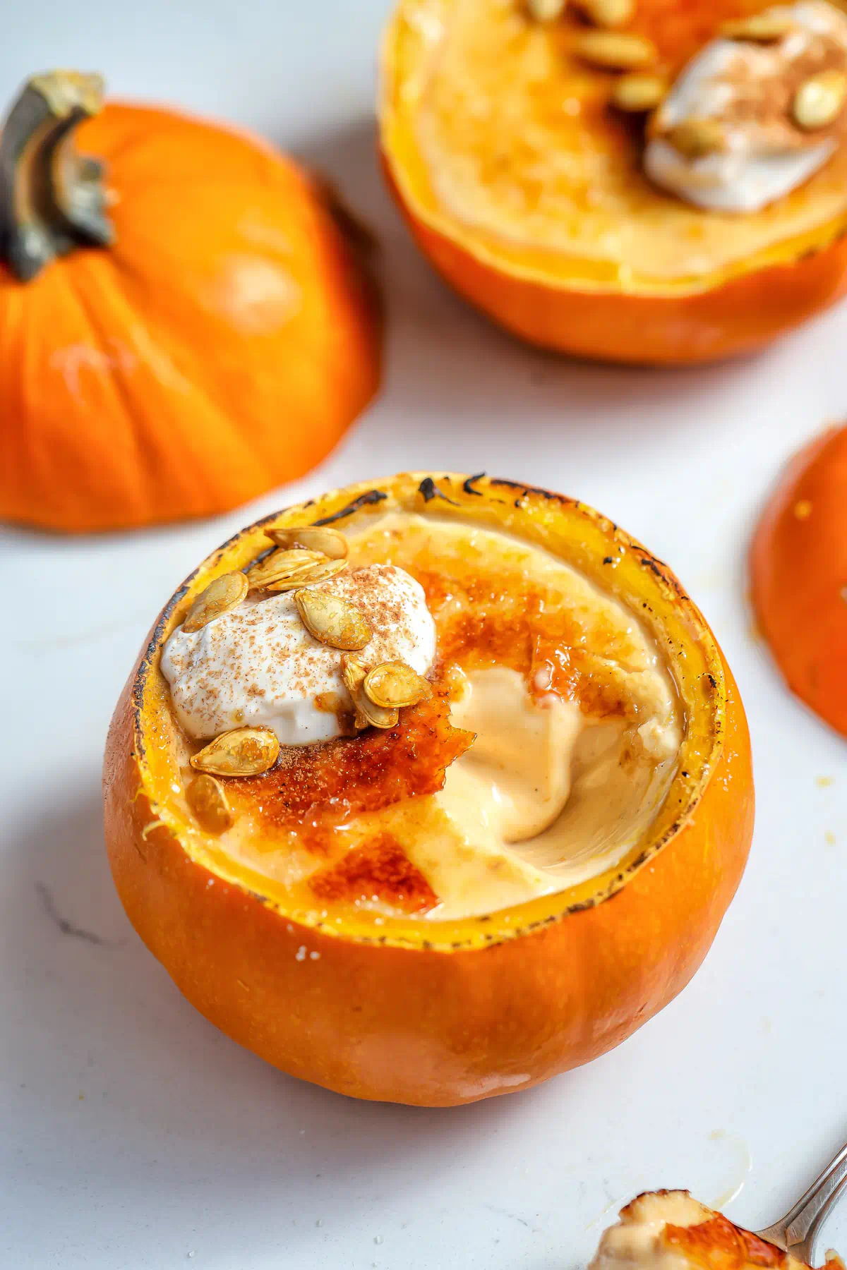 Make-ahead pumpkin panna cotta served in a roasted mini pumpkin with a torched brûlée crust, cinnamon whipped cream, and roasted pumpkin seeds.