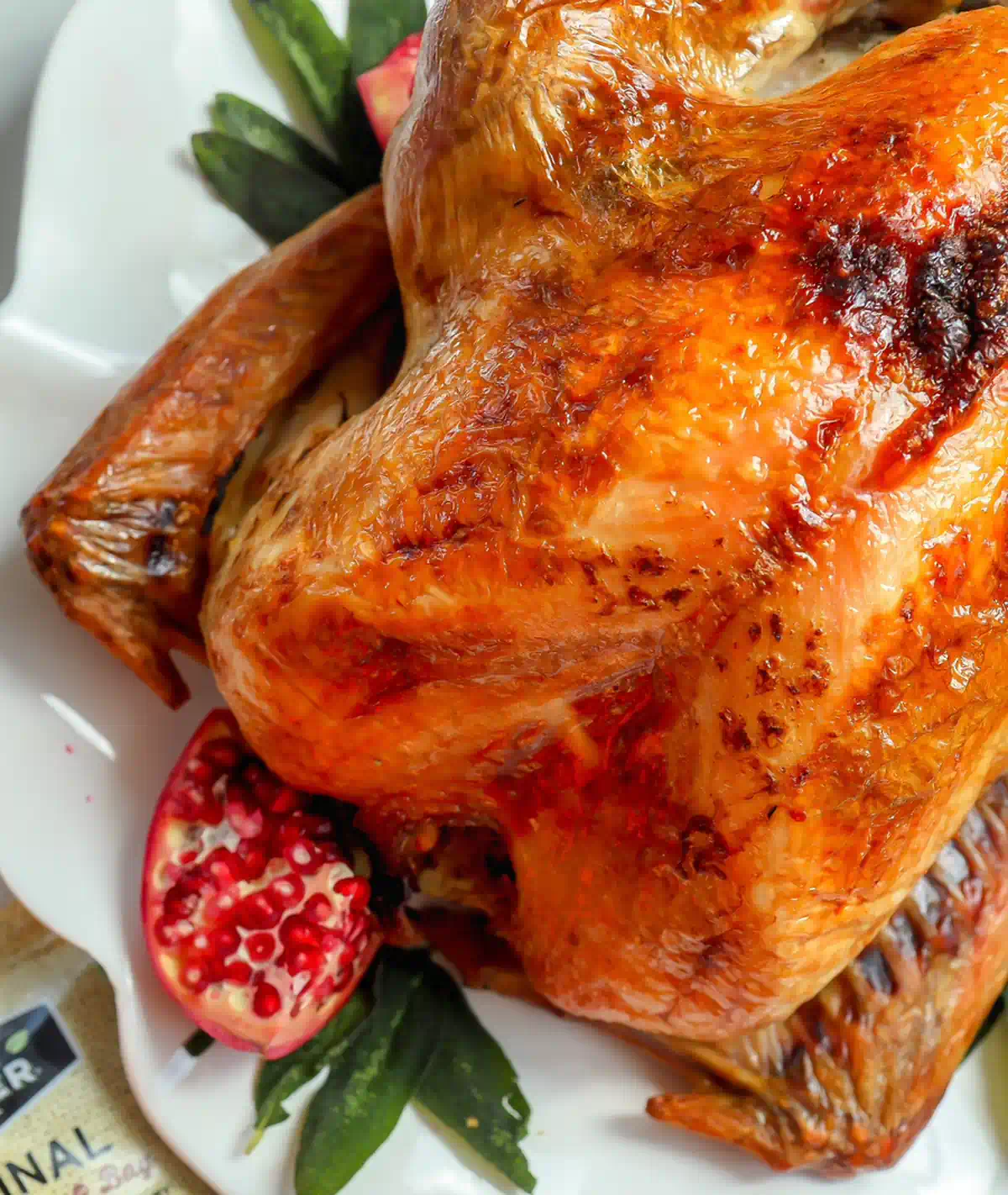 Close up of a roasted turkey breast and wing with deeply browned skin, with a halved pomegranate and sage leaves on the platter
