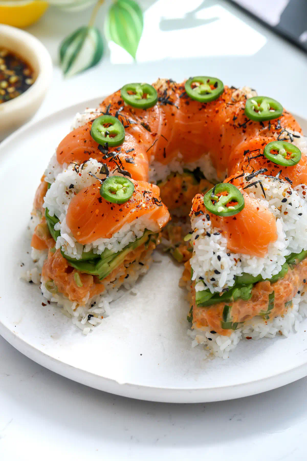 A slice of salmon sushi cake removed showing the internal layers of velvety avocado, crisp Persian cucumber, and the creamy spicy salmon mixture.