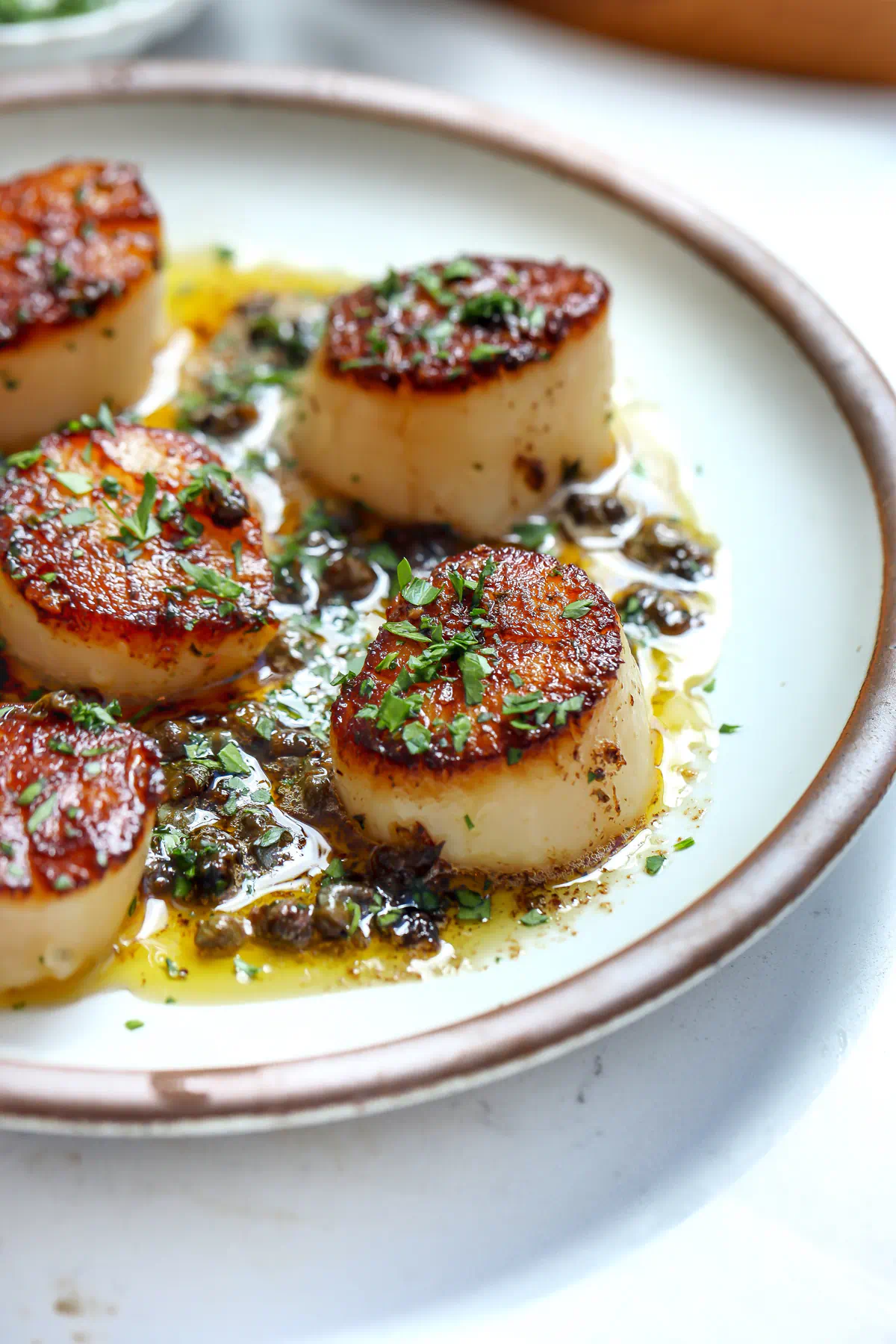 Pan-seared scallops meunière on a white plate with lemon caper butter sauce and chopped fresh herbs