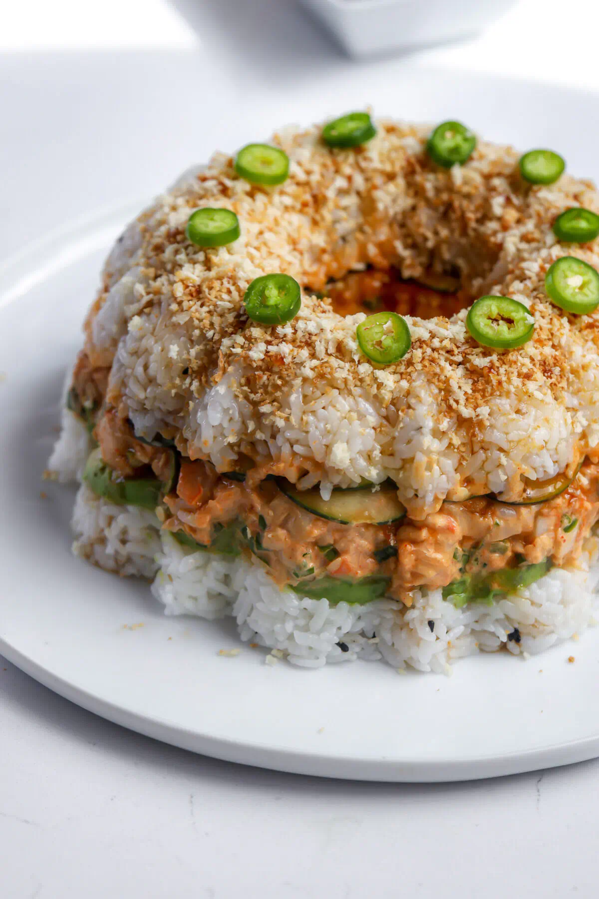 Shrimp sushi bundt cake topped with toasted panko, serrano slices, and unagi sauce.