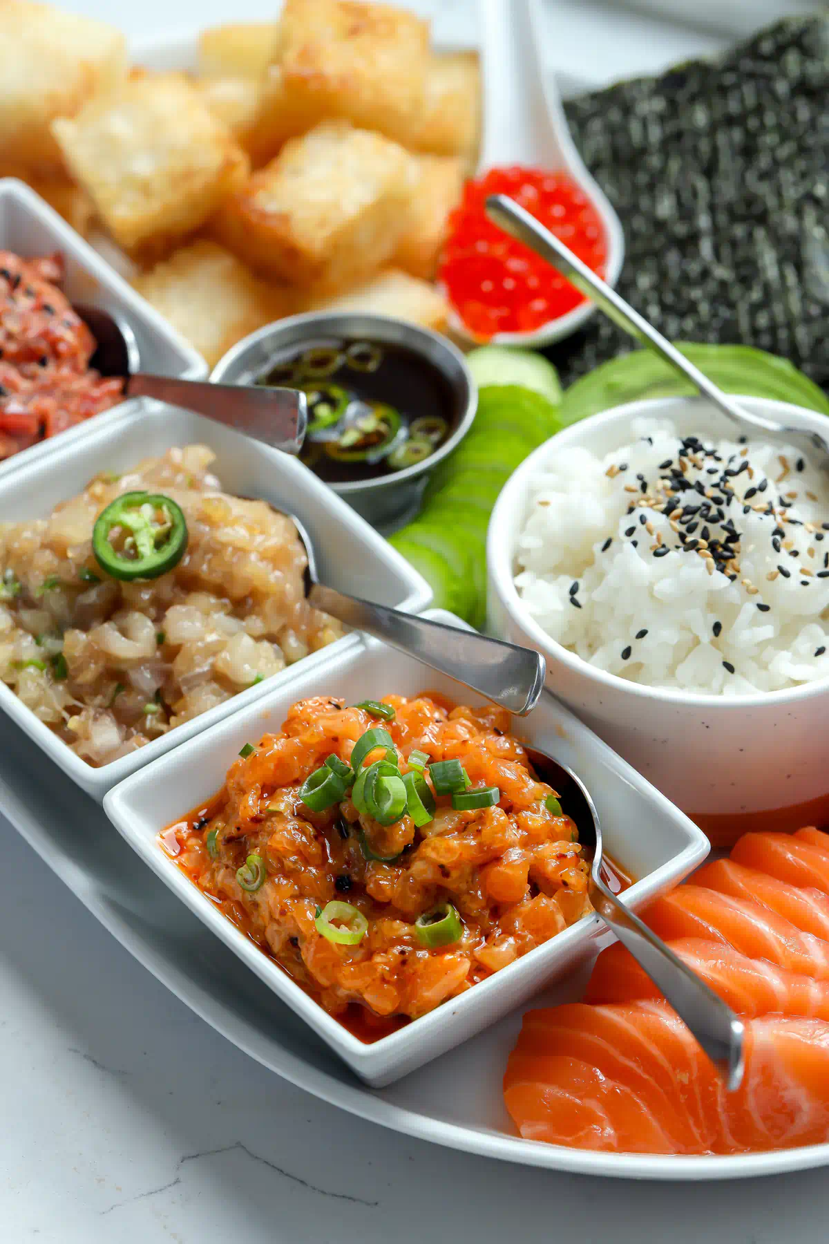 Salmon, tuna, and yellowtail sashimi fanned beside a bowl of sushi rice topped with black and white sesame seeds on a sushi board.