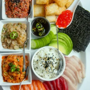 Full sushi charcuterie board from above with fried sushi rice cubes, spicy tuna, salsa macha salmon, yuzu jalapeño yellowtail, jalapeño ponzu, sushi rice, and sliced sashimi.