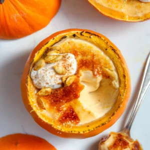 Overhead of pumpkin panna cotta in a hollowed mini pumpkin, brûléed sugar top cracked open, cinnamon whipped cream and roasted pumpkin seeds, whole pumpkins alongside.