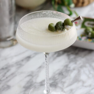 An easy quick vodka cocktail, this Milky Dirty Martini is sitting in a chilled glass with stuff fog cheese olives skewered as garnish.