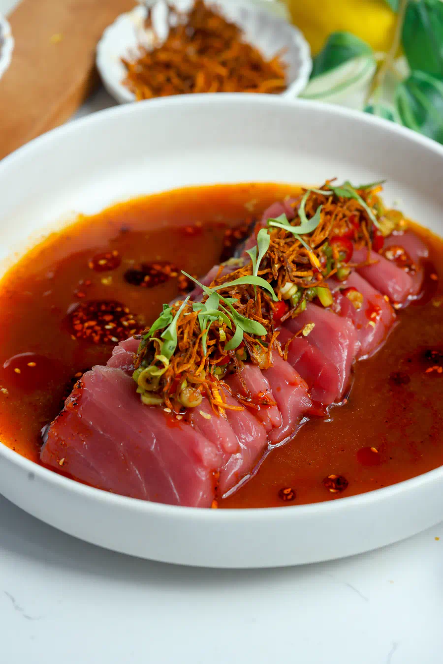 Angled close up of spicy tuna crudo with shoyu ponzu sauce and golden fried carrot matchsticks.