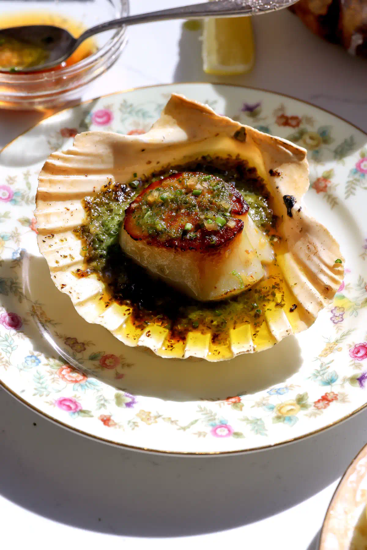 Golden brown seared scallops in a shell with escargot butter broiled on top at an angle.