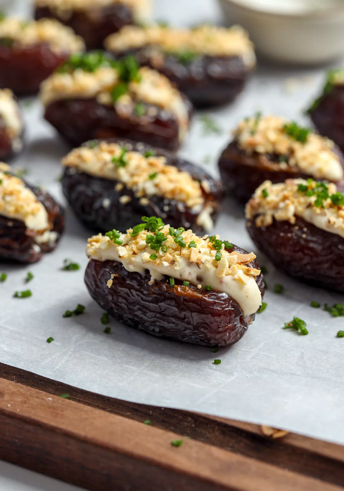 Close-up portrait macro shot of a single Medjool date stuffed with whipped brie, topped with toasted crushed almonds and fresh minced chives.