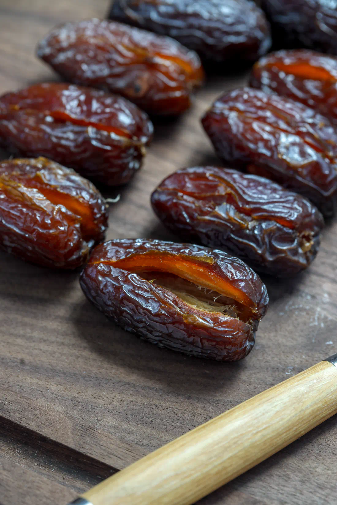 Rows of raw Medjool dates, sliced open lengthwise with the pits removed, sitting on a dark wooden cutting board.