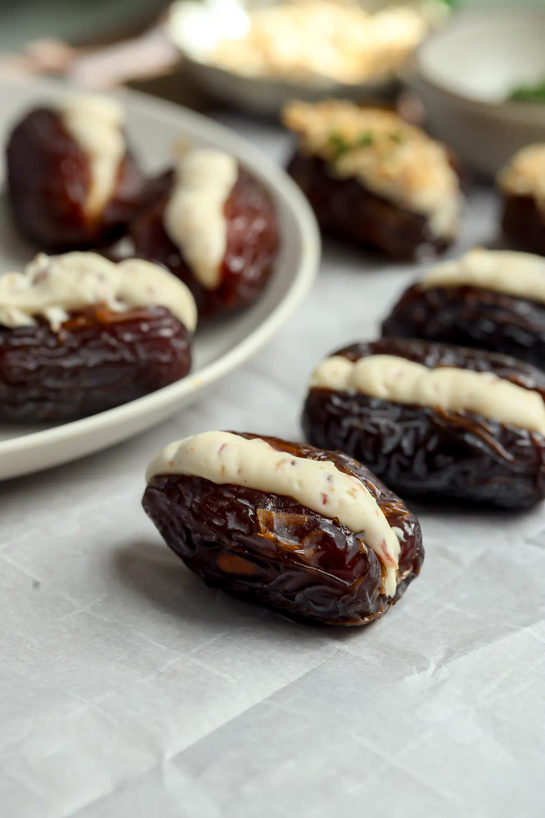Pitted Medjool dates on parchment paper with a neat stripe of whipped brie and bacon filling before the final topping.