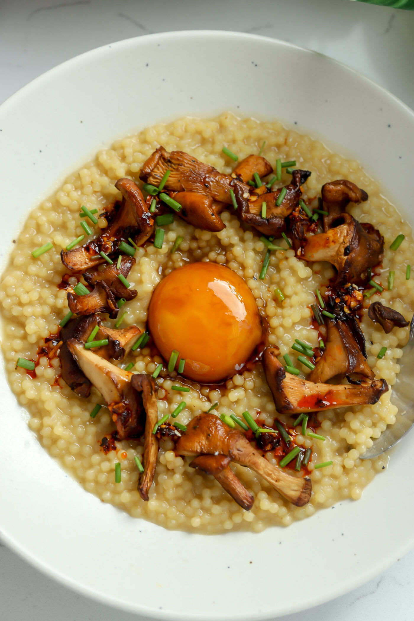 Pastina in a bowl topped with caramelized chanterelle mushrooms, cured egg yolk and chives.