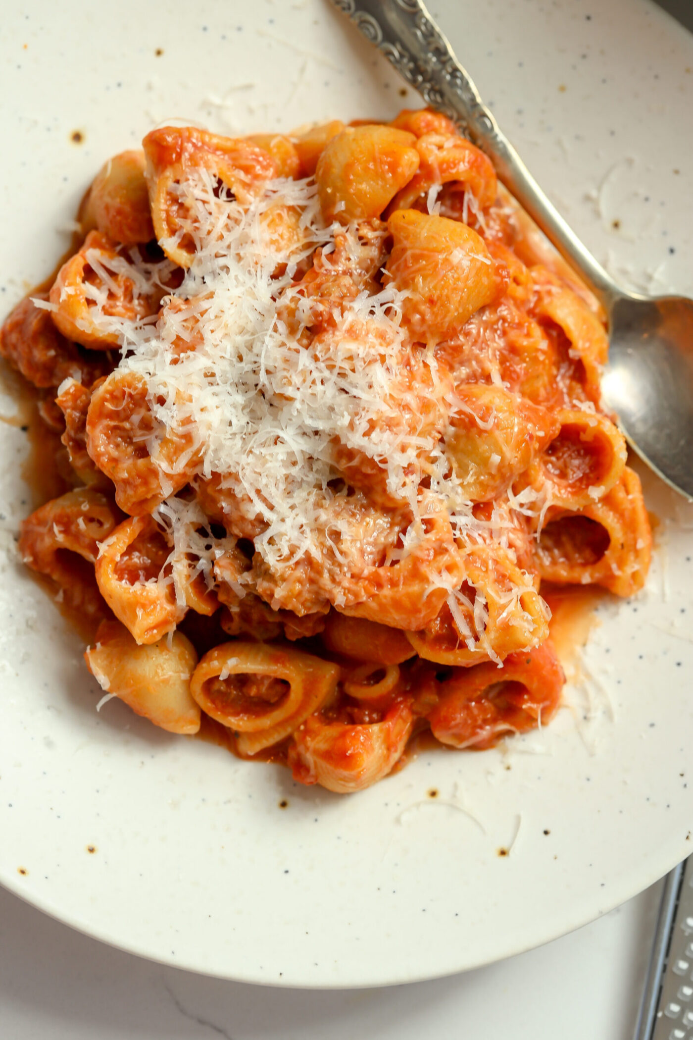Creamy tomato sauce coating the pasta shells. A generous amount of parmesan cheese is sitting on top with a spoon sitting next to it.