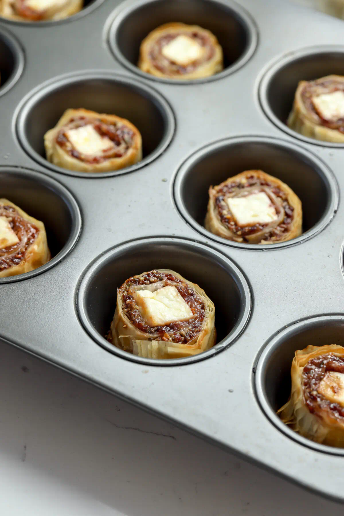 Assembled feta and cranberry bites in a muffin tin before baking, each showing a square of feta in the center