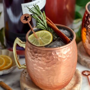 This London Mule is nice a fizzy in a copper cup and garnished with a slice of lemon, rosemary and a cinnamon stick with Impress Gin in the background.