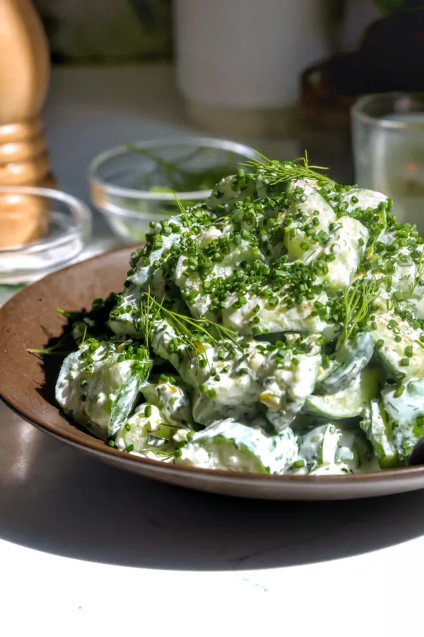 creamy ranch cucumber salad with smashed persian cucumbers topped with fresh chives, dill, and cracked black pepper on a brown plate