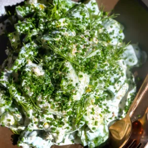 overhead view of creamy ranch cucumber salad piled with finely chopped chives and dill fronds