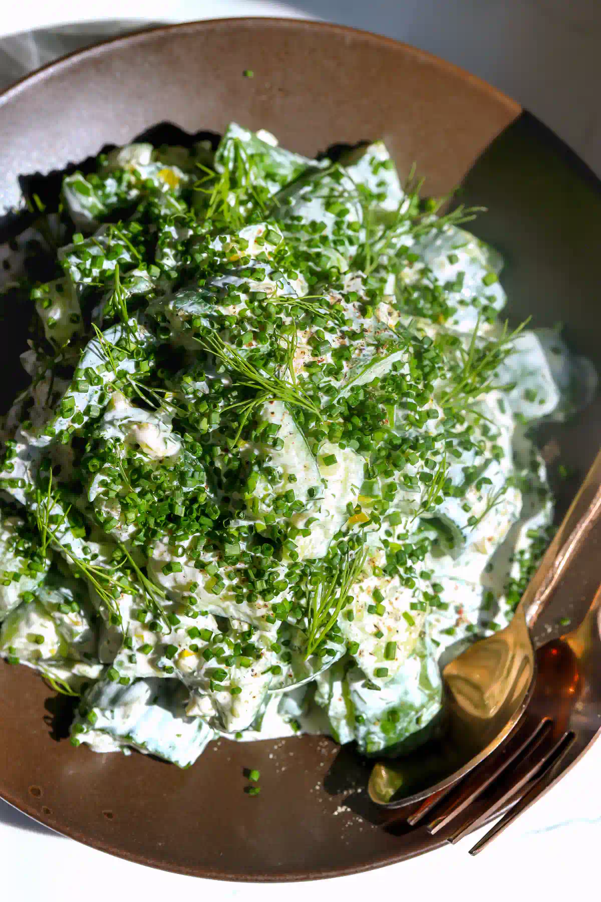 overhead view of creamy ranch cucumber salad piled with finely chopped chives and dill fronds