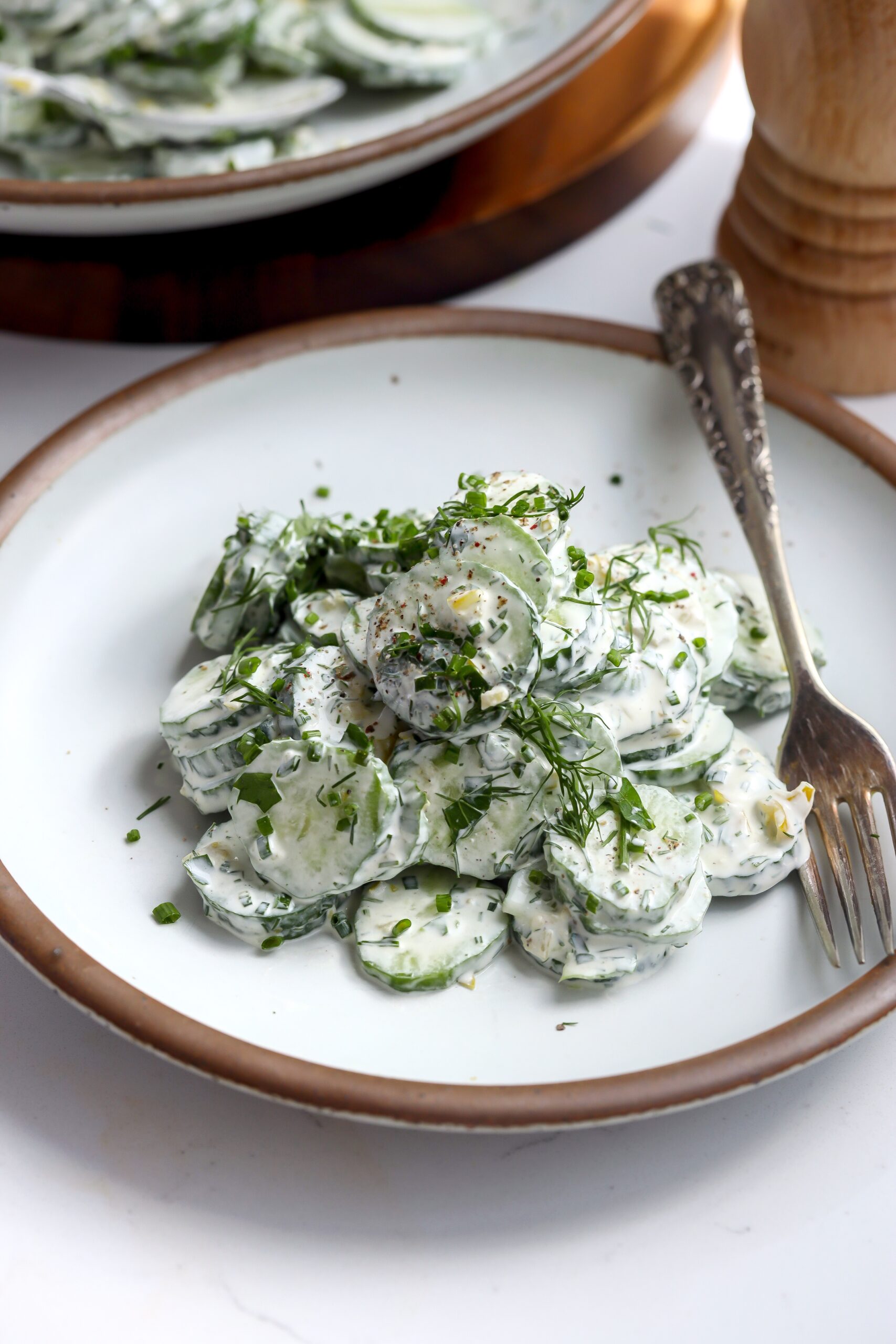 sliced cucumbers on a plate with a creamy pepperoncini ranch sauce and fresh dill coating it in this delicious recipe.