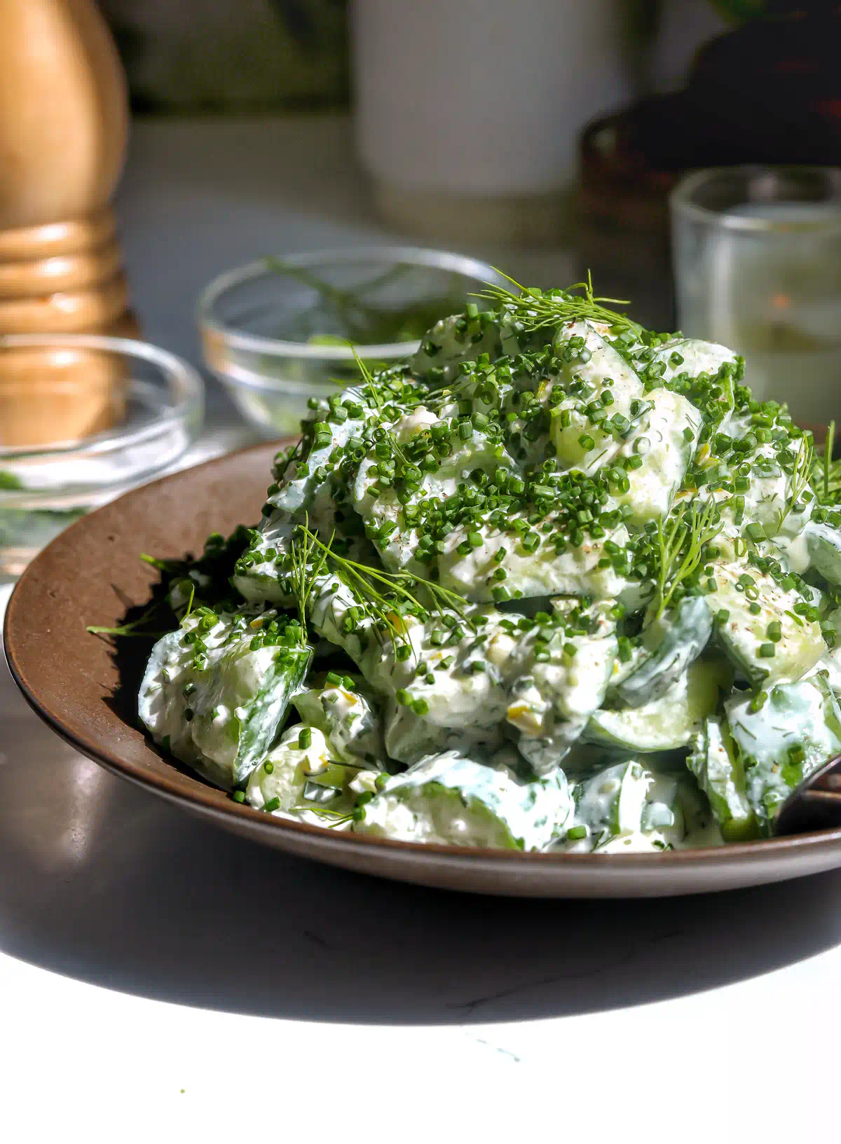creamy ranch cucumber salad with smashed persian cucumbers topped with fresh chives, dill, and cracked black pepper on a brown plate