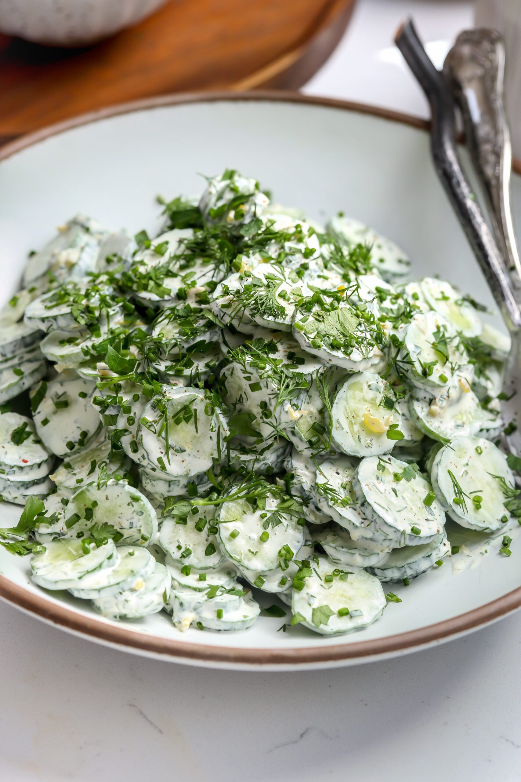 sliced cucumbers on a plate with a pepperoncini ranch sauce and fresh dill coating it in this delicious recipe.