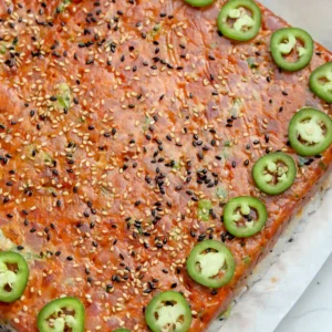 Overhead view of spicy tuna pressed sushi on parchment, topped with black and white sesame seeds and a border of sliced jalape&ntilde;os.