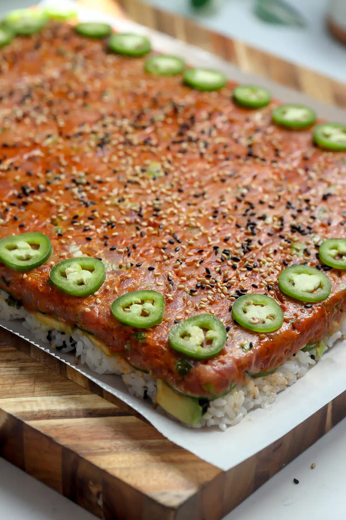 Side view of spicy tuna pressed sushi showing layers of seasoned rice, avocado, and cucumber under the gochujang tuna, oshizushi style.