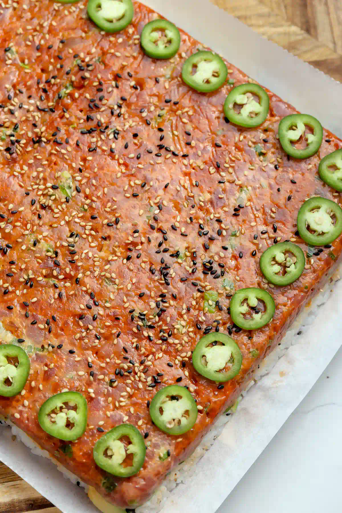 Overhead view of spicy tuna pressed sushi on parchment, topped with black and white sesame seeds and a border of sliced jalape&ntilde;os.
