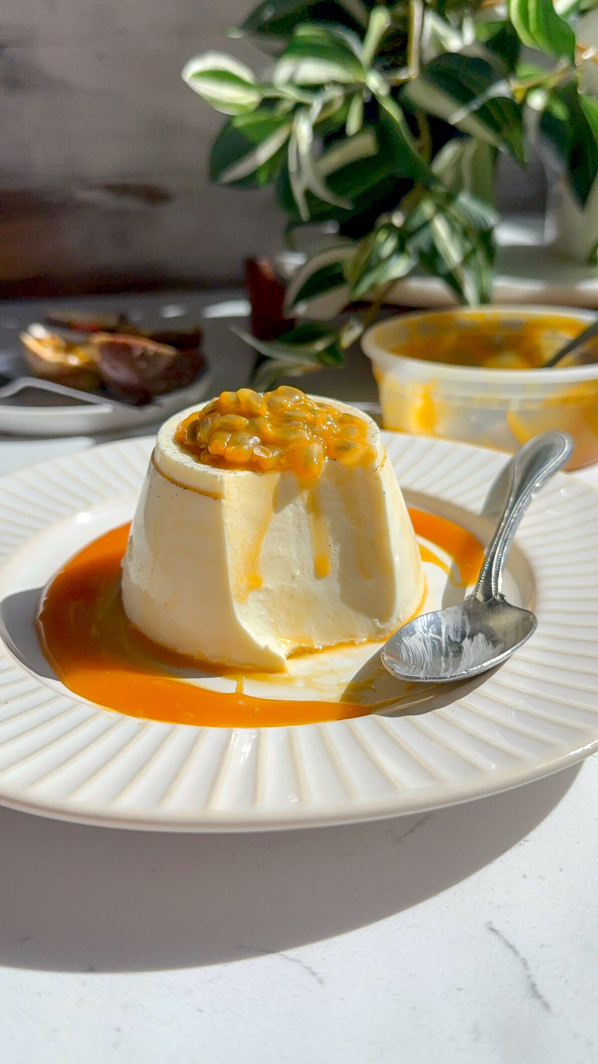 Creamy smooth Panna Cotta with a passion fruit caramel topping with a spoon next to it and a piece taken out to show how creamy the middle is.