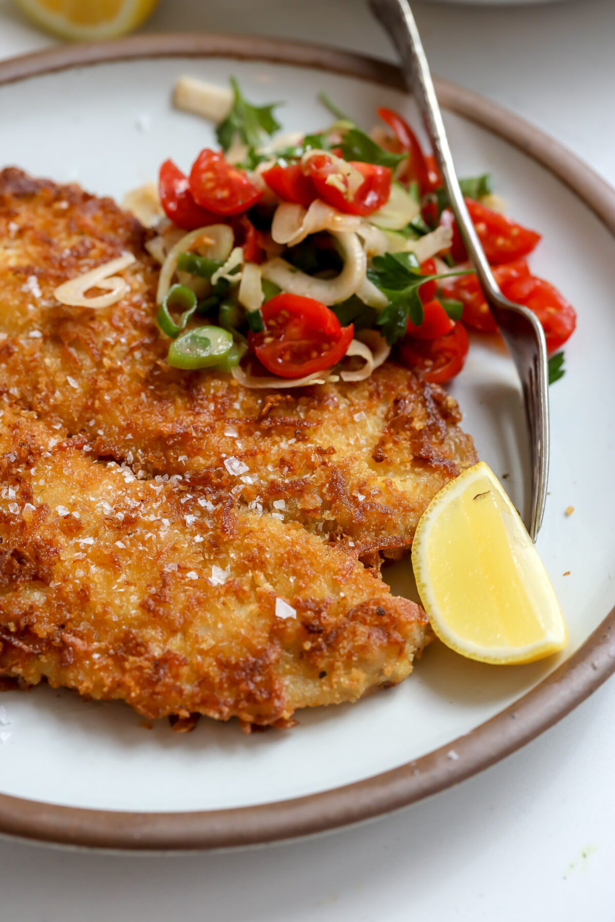 A potato and panko crusted and then pan fried petrale sole filet recipe with a tomato fennel salad, lemon and fork on the plate next to it.