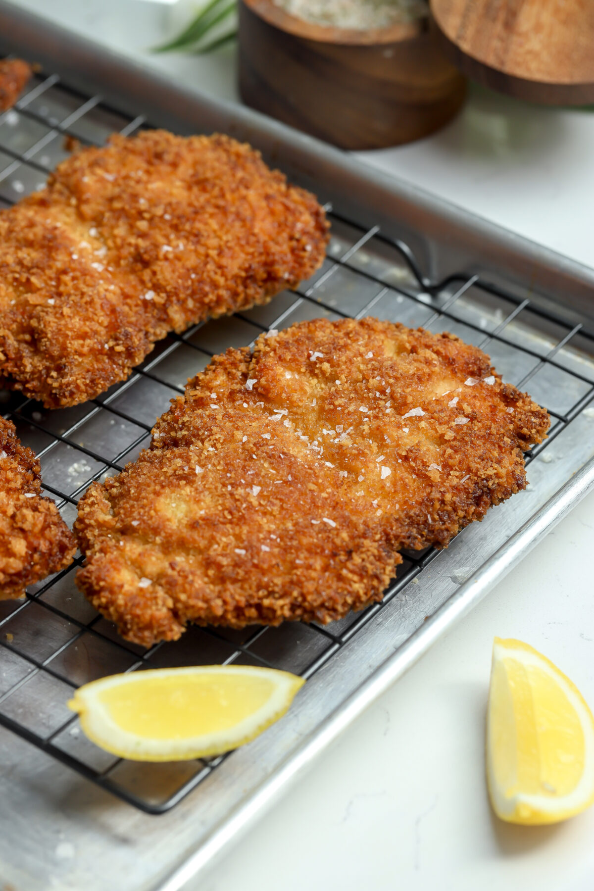 the crispiest chicken ever cooling on a rack with a sprinkle of flakey salt and lemon wedges next to it.