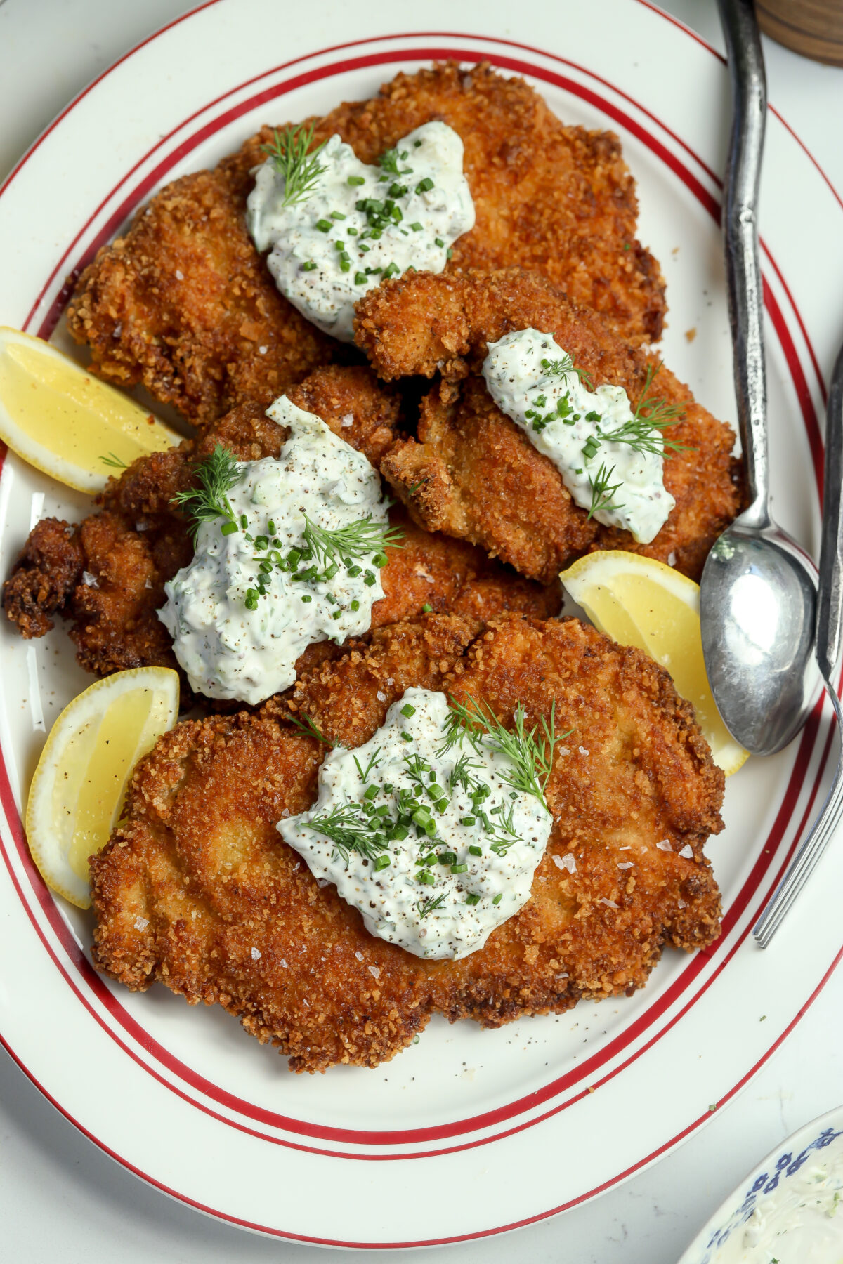 Super crispy chicken recipe with a creamy dollop of dill sauce and chives on top plated next to a lemon and silverware.