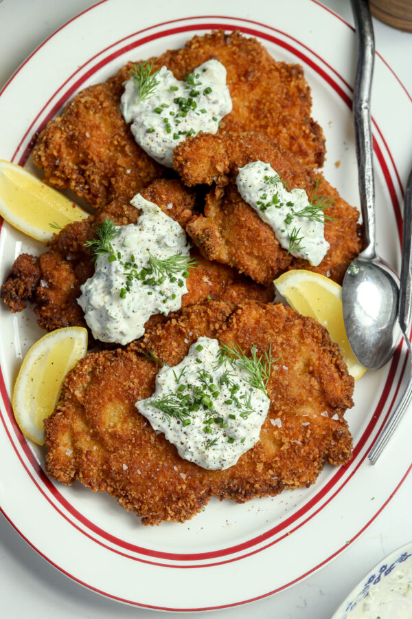 Super crispy chicken recipe with a creamy dollop of dill sauce and chives on top plated next to a lemon and silverware.