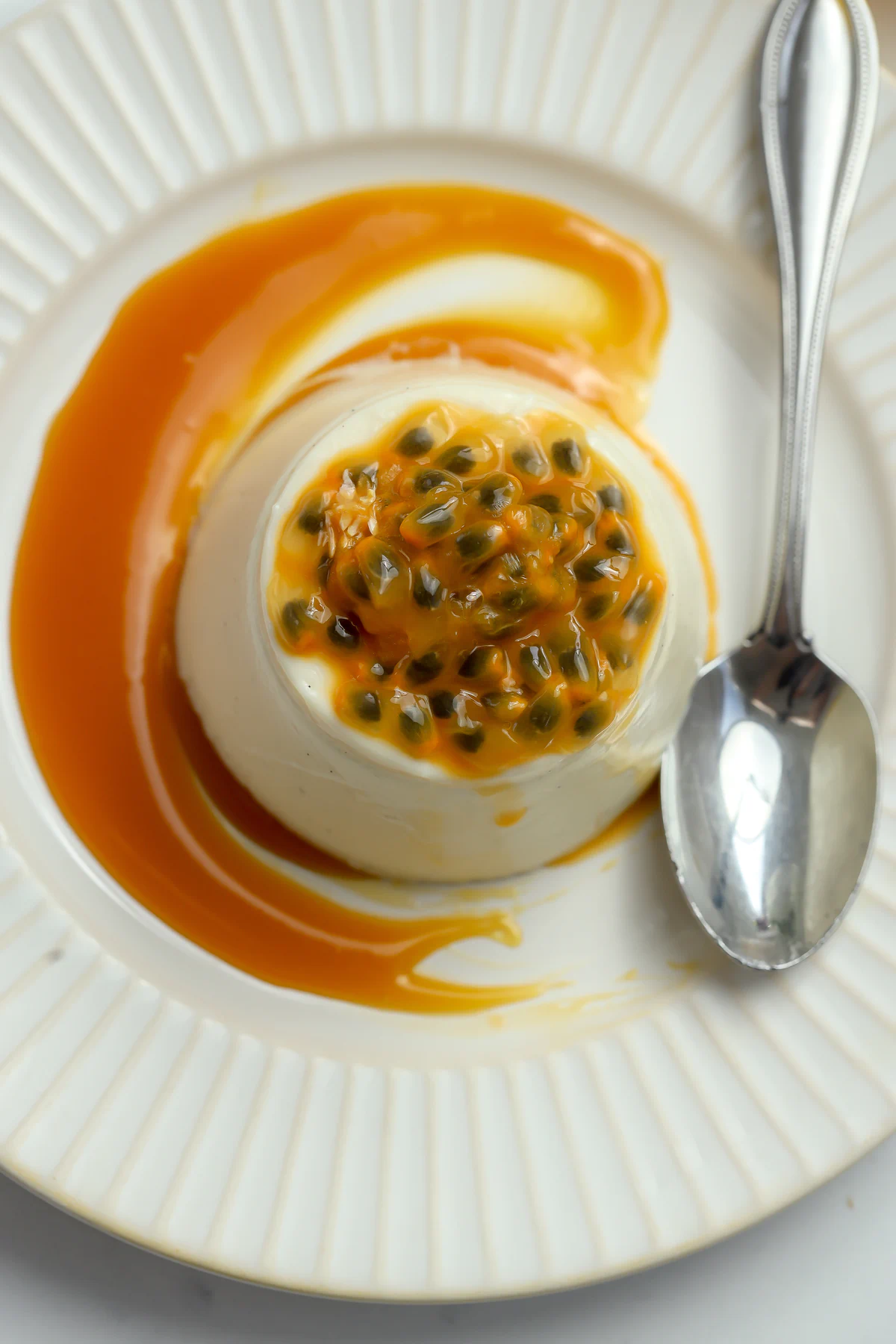 Overhead view of passionfruit caramel panna cotta on a fluted white plate, topped with fresh passion fruit pulp and ringed with orange caramel