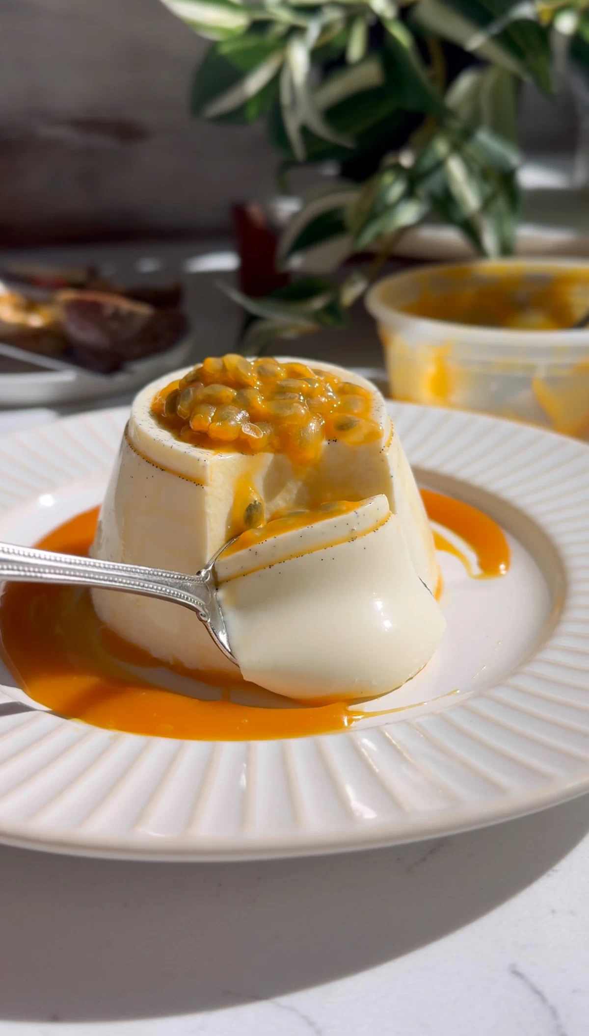 Spoon lifting a bite from a vanilla bean passionfruit panna cotta, passion fruit pulp on top and caramel pooled around the base.