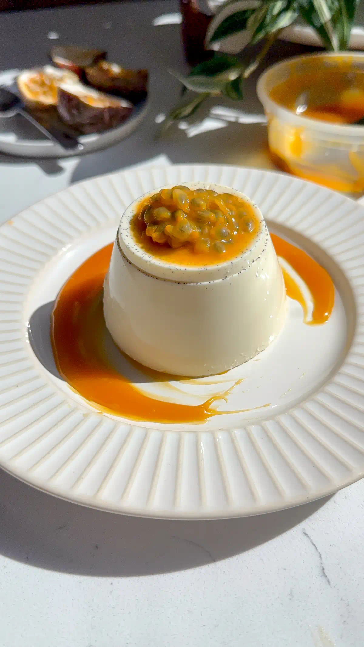 Unmolded passionfruit caramel panna cotta flecked with vanilla bean, fresh passion fruit on top and caramel pooled on a white plate.