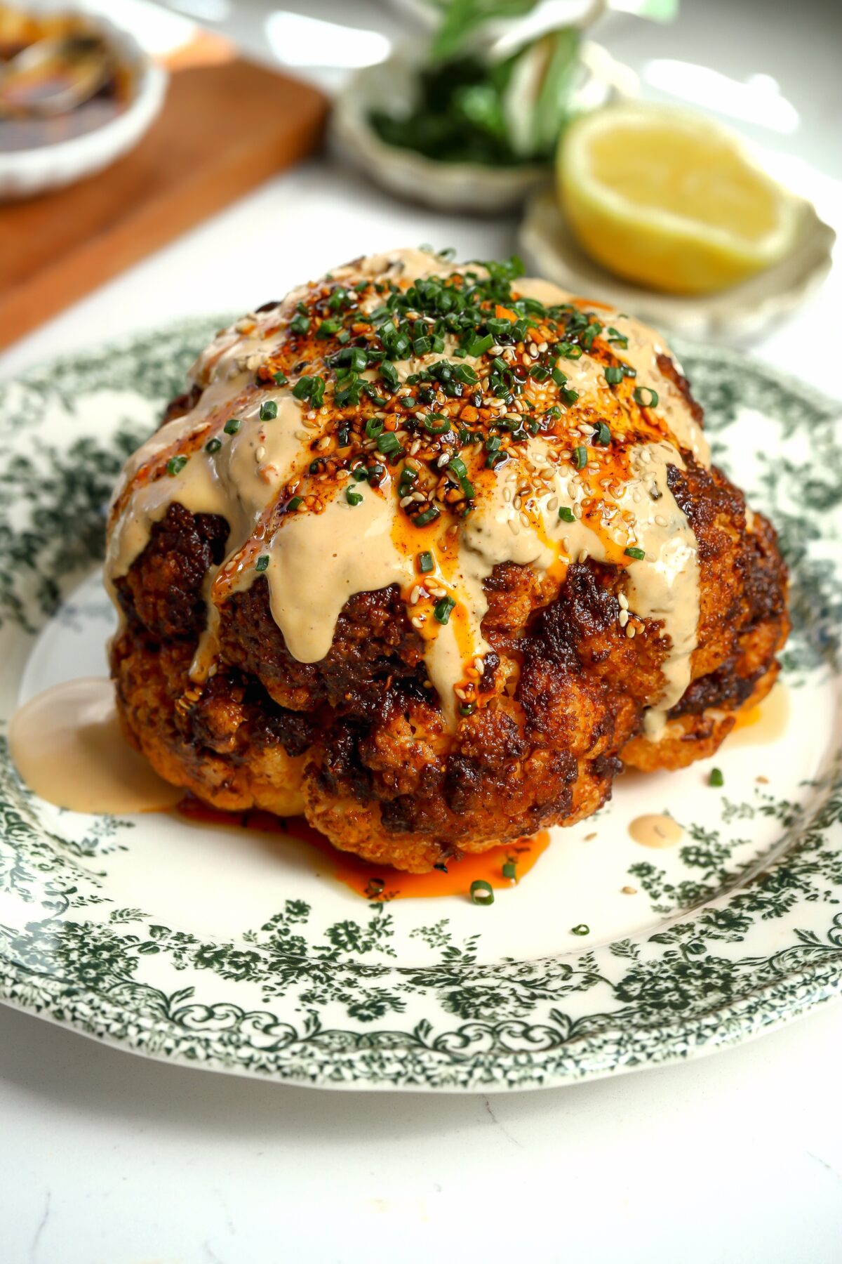 Whole head of roasted cauliflower covered in a creamy miso tahini sauce, topped with chives sitting on a plates