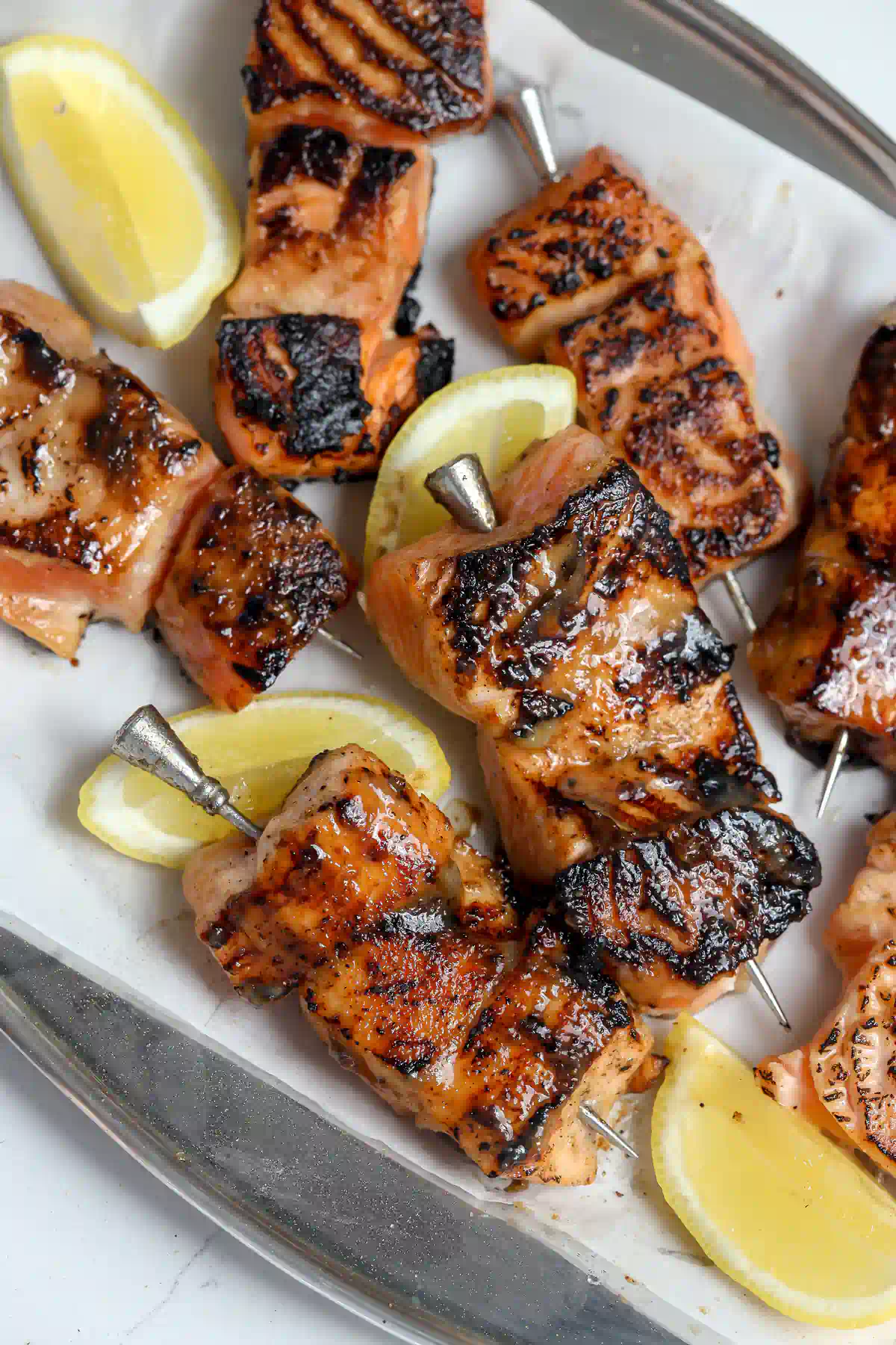 Close-up of cubed miso salmon skewers on a metal platter, showing the caramelized, charred miso glaze and a lemon wedge.