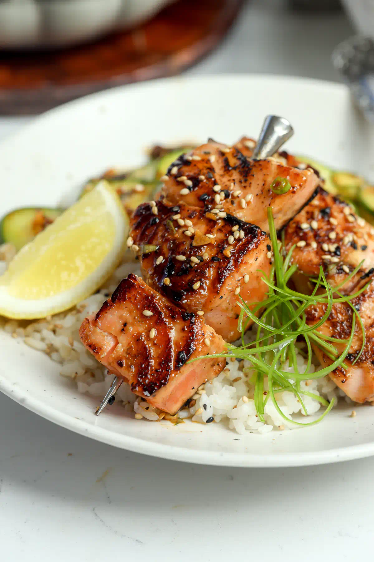 Miso salmon skewers over white rice, topped with sesame seeds and curled scallion, with a lemon wedge alongside.